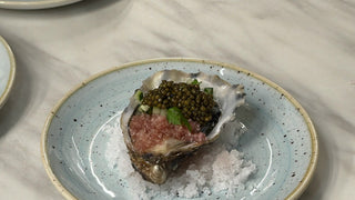 An oyster on a bed of salt on a pale blue plate, topped with Royal Oscietra caviar, red wine vinaigrette and diced cucumber.